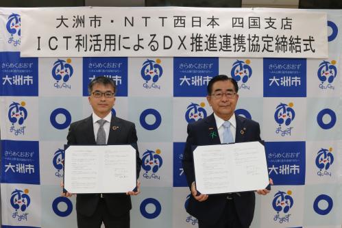 NTT西日本四国支店長と大洲市長がそれぞれ協定書を持って正面を向いている写真