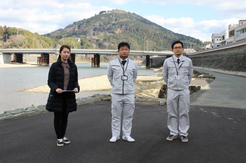 肱川のほとりで一人のアナウンサーと二人の市職員が立っている写真