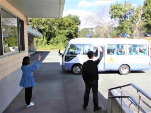 バスで次の場所に向かう子ども達に所長と栄養教諭が手を振る様子